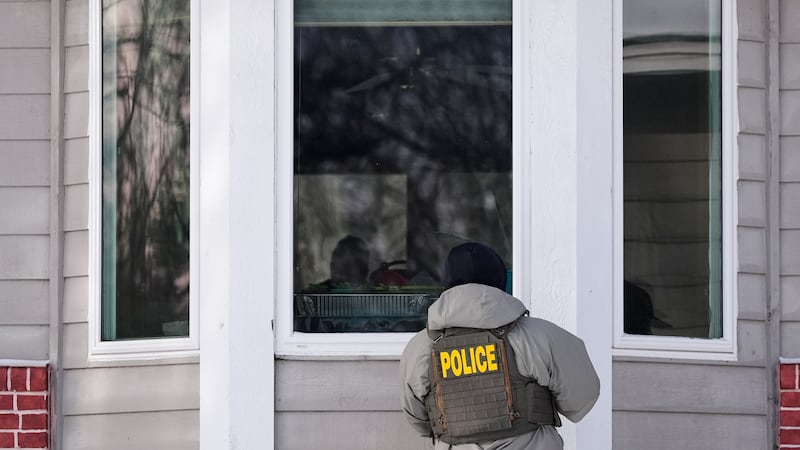 Un agente federal de inmigración mira por la ventana de una casa el martes 20 de enero de 2026...